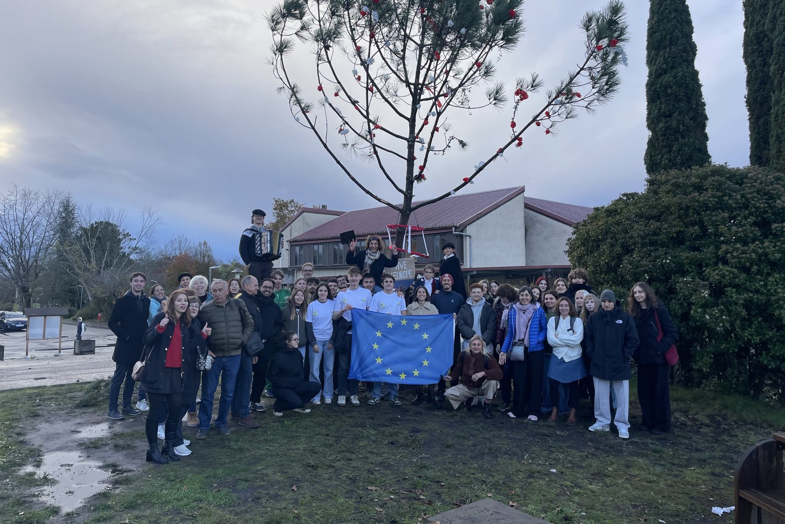 A large group of seminar participants and students holding a European flag under a decorated pine tree