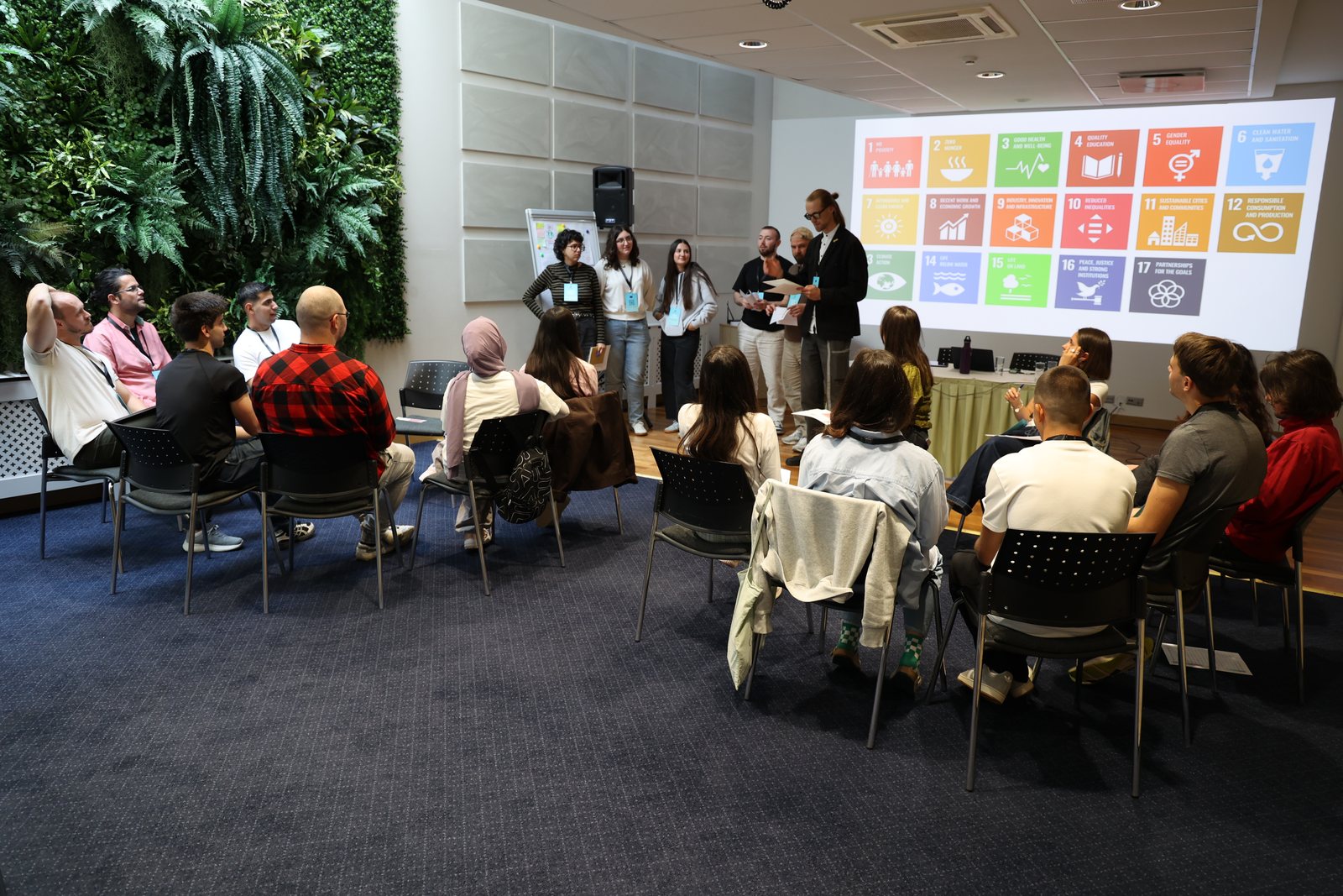 A group presents to other participants in front of a projection of the 17 Sustainable Development Goals