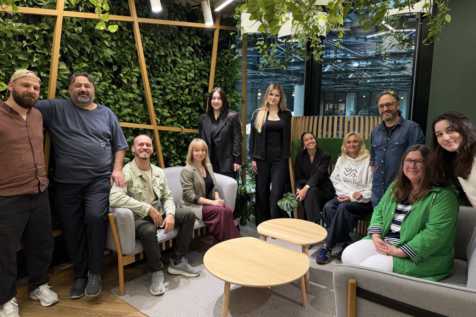 The partners sit and stand together in a lounge with a green plant wall